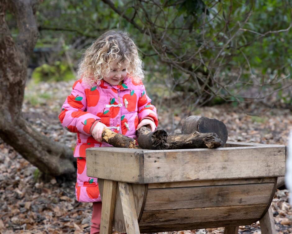 Girl playing with logs and branches in woodland area