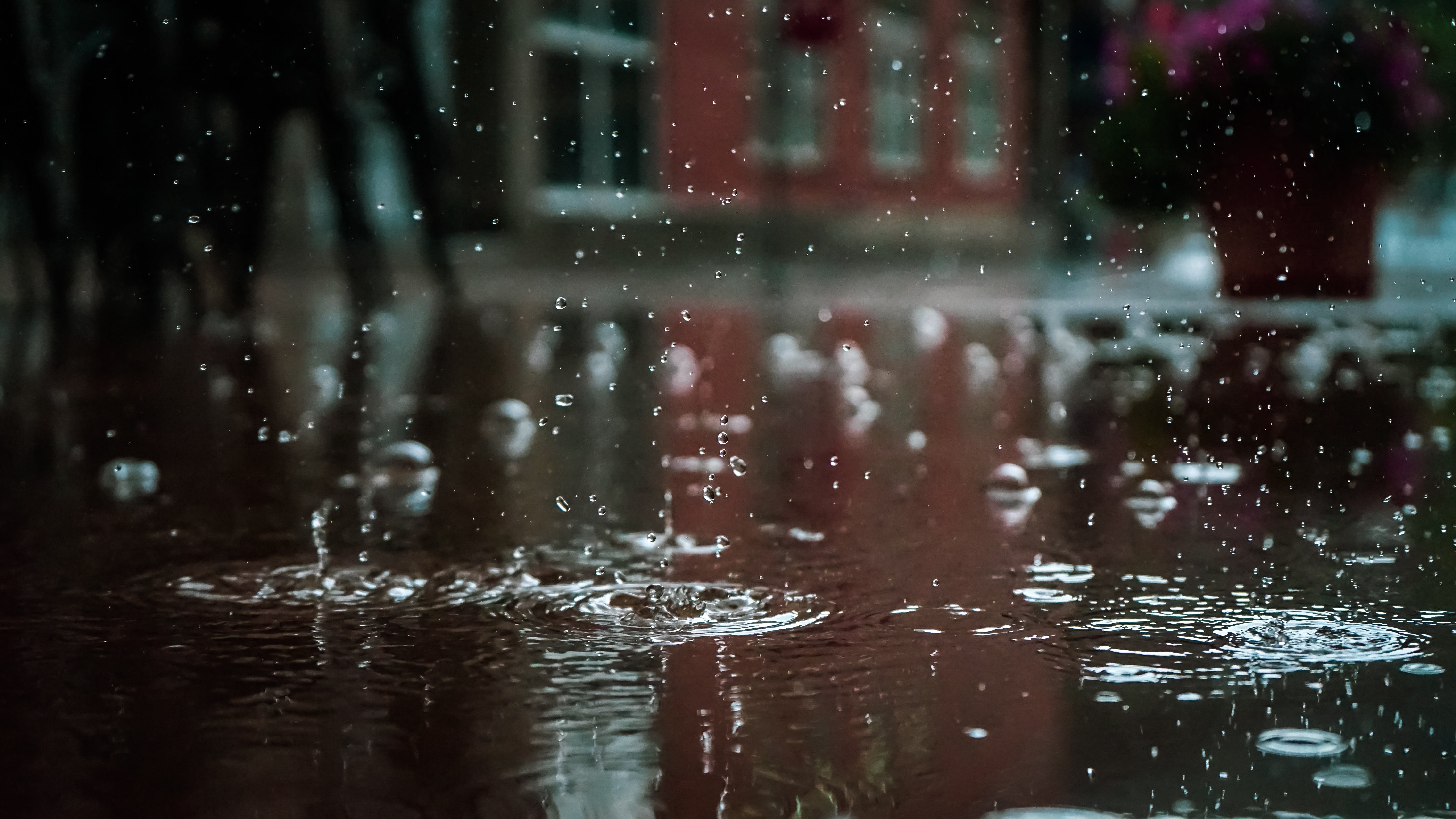 Raindrops splashing ripples into a puddle onto asphalt ground cover