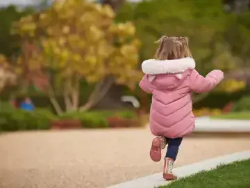 child in pink coat running on the kerb between pavement and some lawn