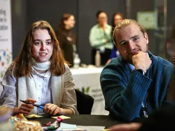 Two teachers facing in conversation with another teacher. Three more people are in the background. A white Nature Park banner is to the side of the room.