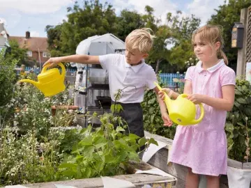 two school children watering plants in a school garden