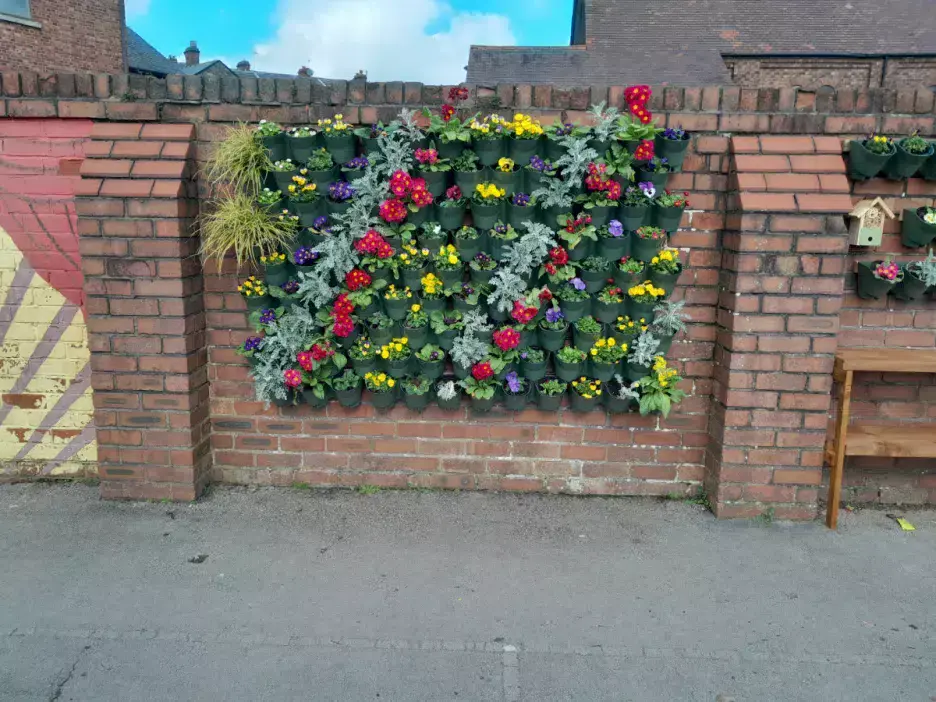 green planters growing on a brick wall with colourful flowers in them 