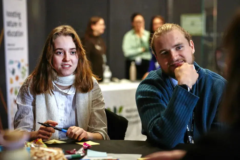 Two teachers facing in conversation with another teacher. Three more people are in the background. A white Nature Park banner is to the side of the room.