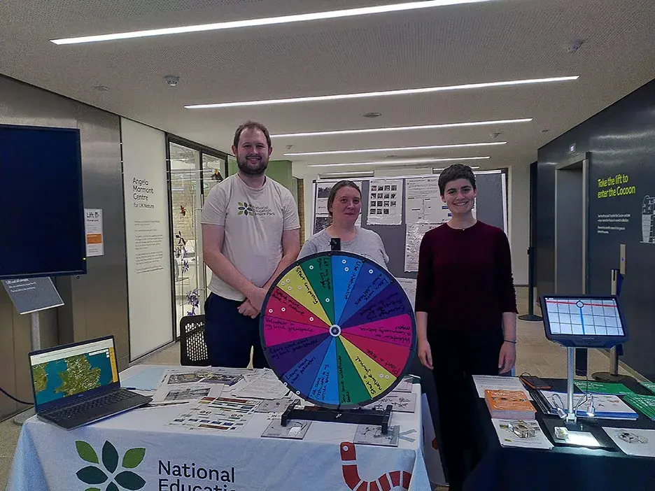 Three scientists at a stand with a colourful wheel on the desk