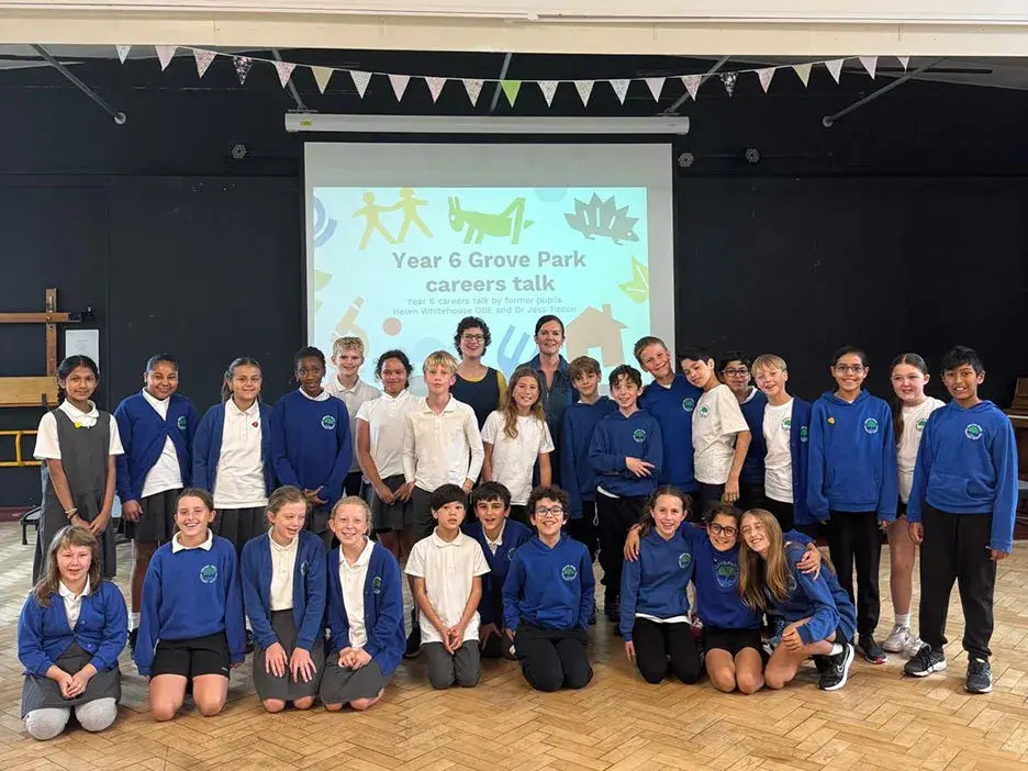 A class stand in front of a screen in assembly with Dr Jess Tipton and Helen Whitehouse