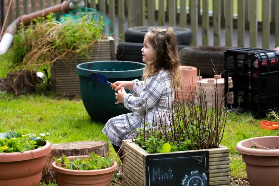 Young child sits in a school garden holding a trowel